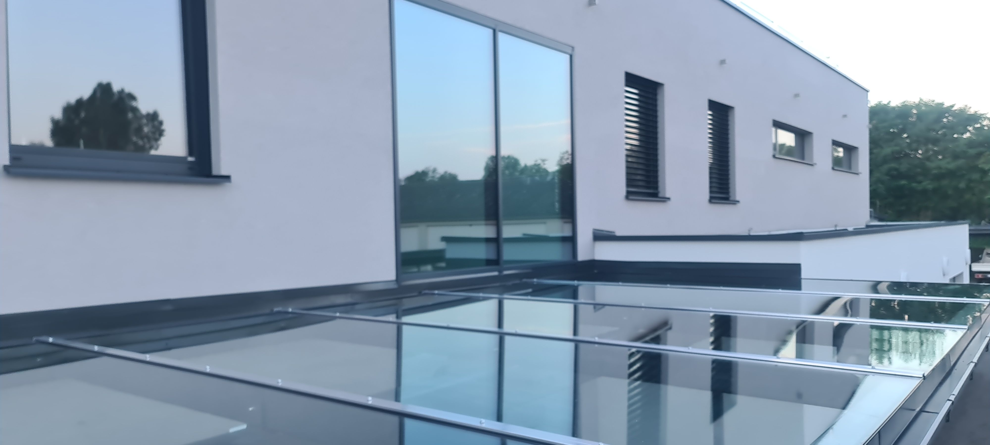 Terrassenüberdachung mit Glasdach und anthrazitfarbener Aluminiumkonstruktion vor modernem Wohnhaus